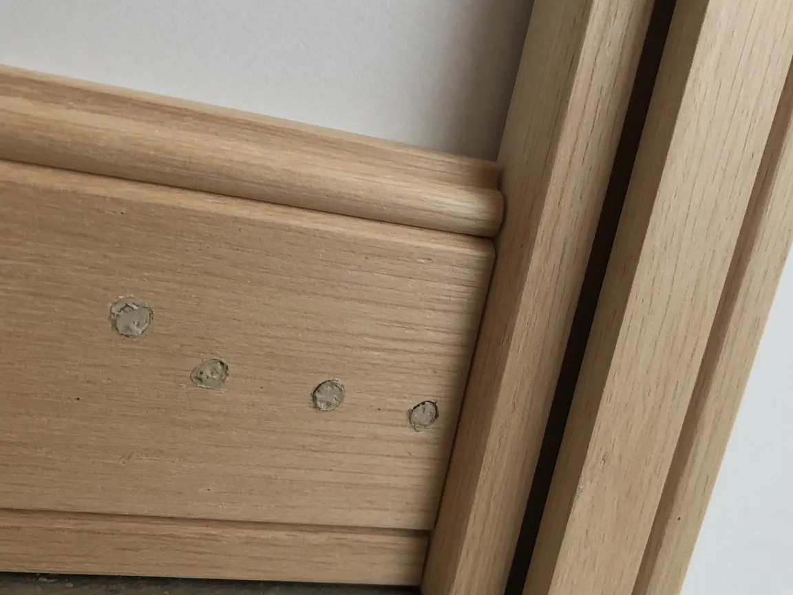 Wooden baseboard with a row of small filled holes from a localized treatment